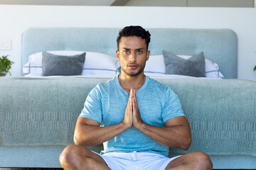 Portrait of biracial man sitting on floor in bedroom, meditating