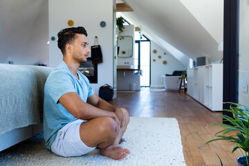 Biracial man sitting on floor in bedroom, meditating