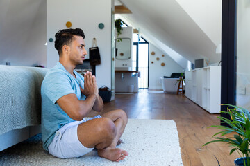 Biracial man sitting on floor in bedroom, meditating