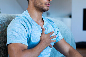 Midsection of biracial man sitting on floor in bedroom, meditating with deep beathing