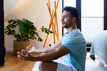 Biracial man sitting on floor in bedroom, meditating
