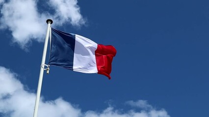 The French flag flutters in the wind against a blue sky with white floating clouds. Bastille Day and French National Day 14 July concept