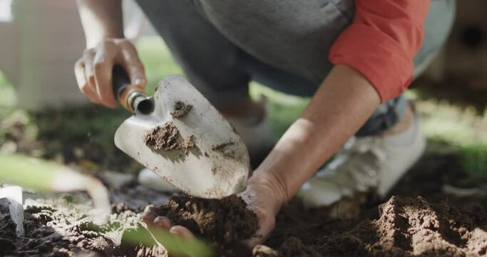 Low section of senior caucasian woman preparing soil with hands and trowel in garden, slow motion