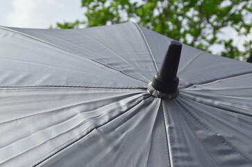 close up of a silver open umbrella against a background of leaves and clear sky during the day....
