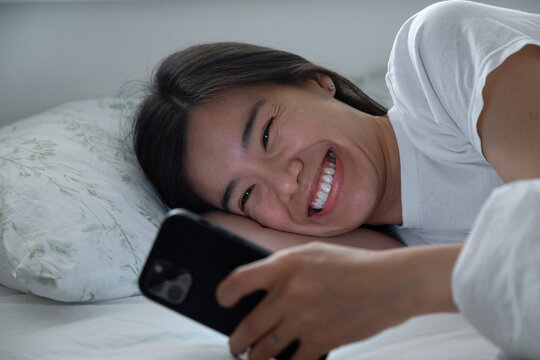 Laughing female with phone chilling in bed