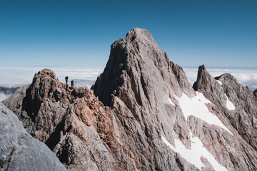 Two climbers doing the rock ridge of Cabrones-Cerredo in Picos de Europa, over a sea of clouds.