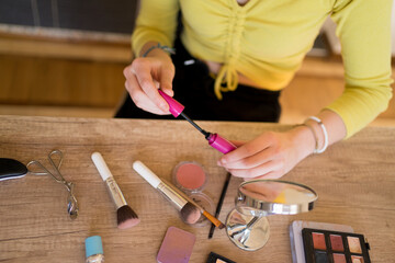 Close-up photo of woman doing her make up on the table in living room.