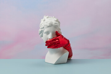 Sculpture with hands in red gloves cover mouth.