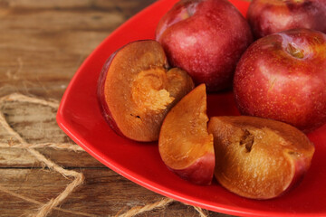 Red plum put in red plastic plate on wooden floor