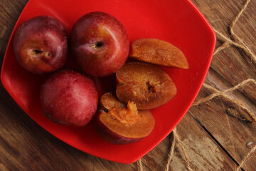 Red plum put in red plastic plate on wooden floor