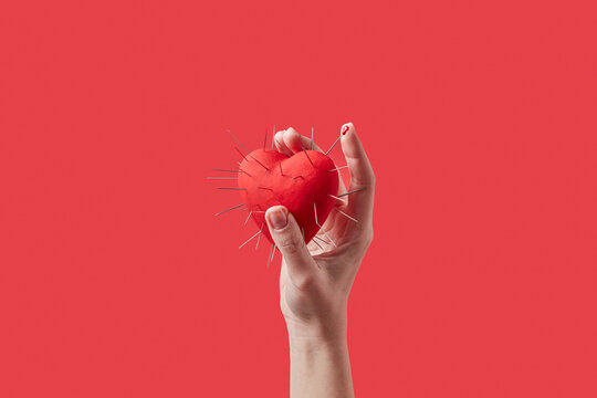 Red heart with metal spikes held by female hand.