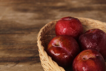 Red plum put in black bamboo basket on wooden floor