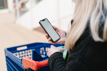 Crop woman using cellphone and pushing trolley
