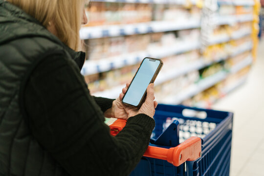 Crop woman browsing cellphone in supermarket