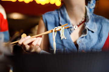 Woman eating delicious ramen using chopsticks at restaurant