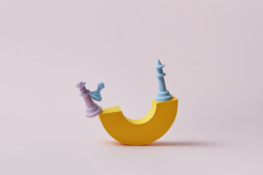 Chess pieces balancing on yellow paper arc.