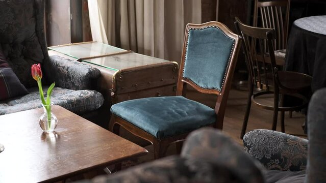 old retro vintage wooden armchair with blue upholstery stands in front of table with flower in old interior. concept of new flower and old furniture, comparison of eras and ages.