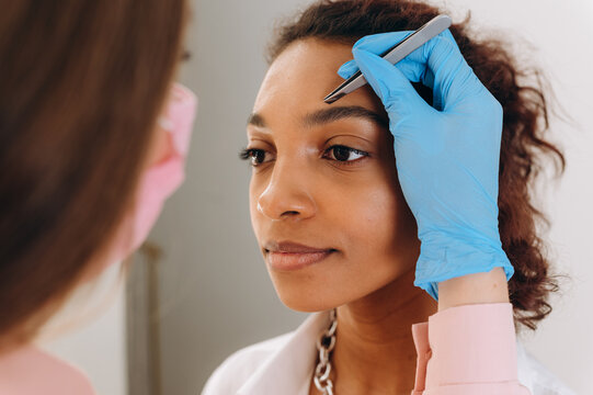 Crop beautician plucking eyebrows with tweezers