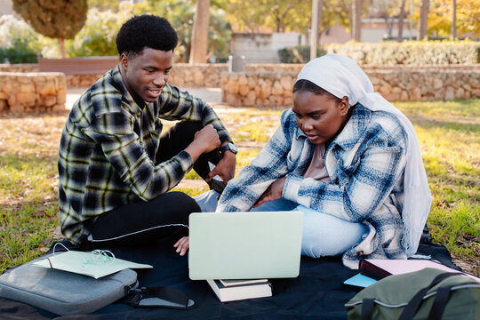 Black students sitting with laptop in a park