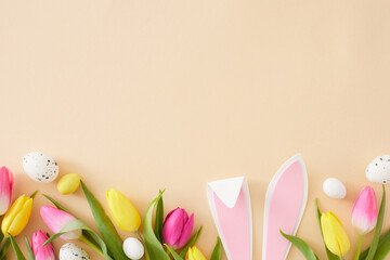 Fototapeta na wymiar Easter concept. Flat lay composition of rabbit bunny ears pink yellow tulips flowers and colorful easter eggs on isolated beige background with copyspace
