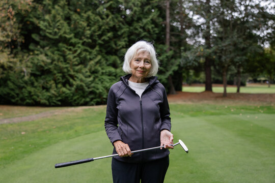 Thoughful portrait of white haired woman holding golf club.