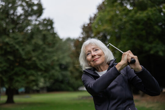 Silver haired woman playing golf on course.