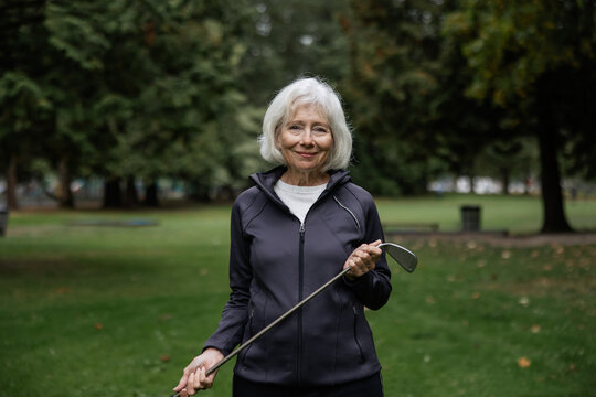 White haired woman smiling at the camera holding golf club.