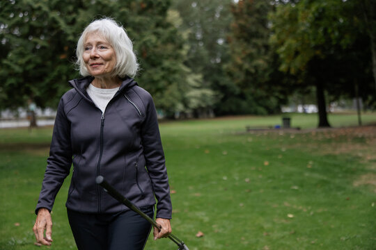 Grey haired woman walking holding golf clubs on course.