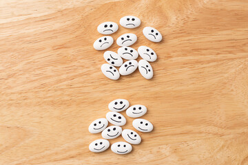 Medicine pill with happy and sad faces over table of wood with copy space