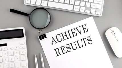 ACHIEVE RESULTS written on paper with office tools and keyboard on the grey background