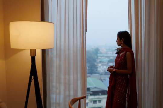 Young woman stands alone by the window at twilight