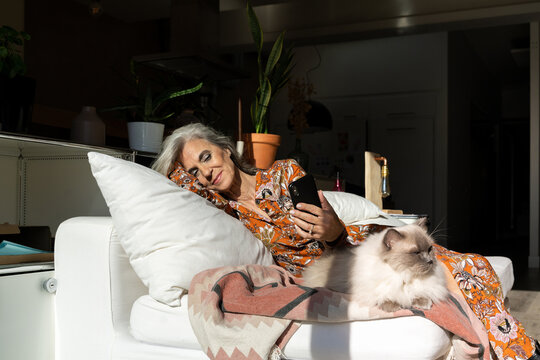Mature woman using phone with cat at home