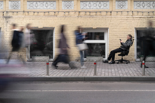Guy sits on sidewalk between walking people blurred in motion