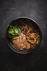 Asian food. Appetizing soup with meat and noodles on a dark background.