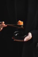 Hand holding sushi roll
chopsticks on a dark background. Japanese food.