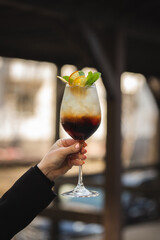 A woman in a black dress holds in her hands a glass of an alcoholic drink with ice in a glass close-up on a dark background