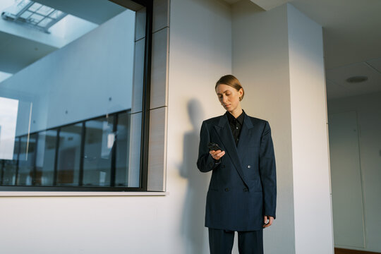  woman wearing man classic suite with  retro cellphone indoors.