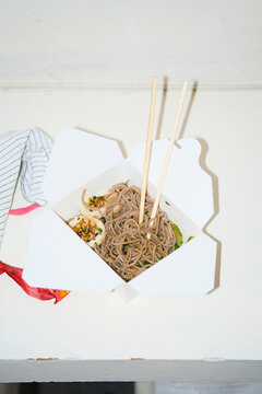 Carton of to-go food noodles and chop sticks on counter top. 