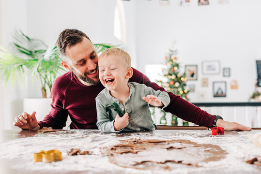 A father and son laughing while baking holiday cookies together