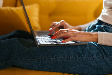 Crop woman typing on laptop on sofa