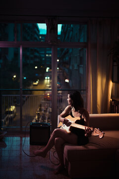 Sitting woman playing guitar in city flat