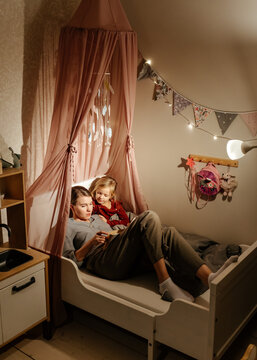 Mother and daughter reading fairy tale in bedroom
