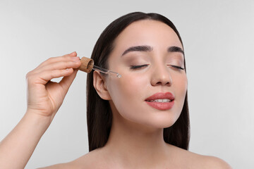 Fototapeta premium Young woman applying essential oil onto face on white background, closeup