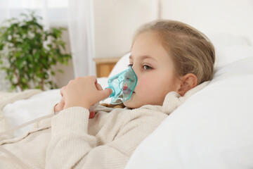 Little girl using nebulizer for inhalation in bedroom