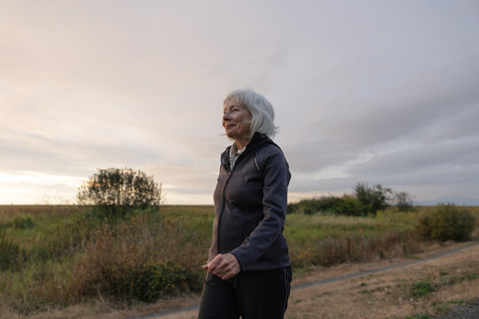 White haired woman walking alone on gravel path in nature.