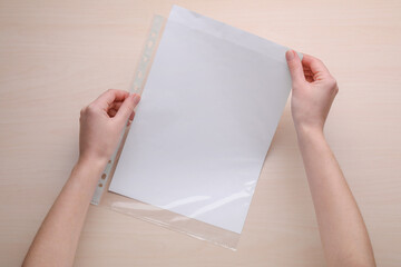 Woman holding punched pocket with paper sheet at wooden table, top view