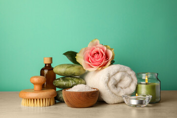 Fototapeta na wymiar Composition with different spa products, candles and rose on beige table against turquoise background