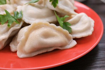 Delicious dumplings (varenyky) with potatoes and parsley on brown wooden table, closeup