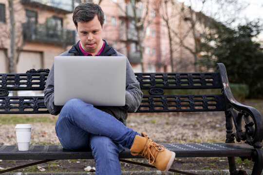 Young man with down syndrome with a laptop in a park