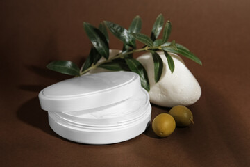 Jar of natural cream, stone and olives on brown background. Cosmetic products